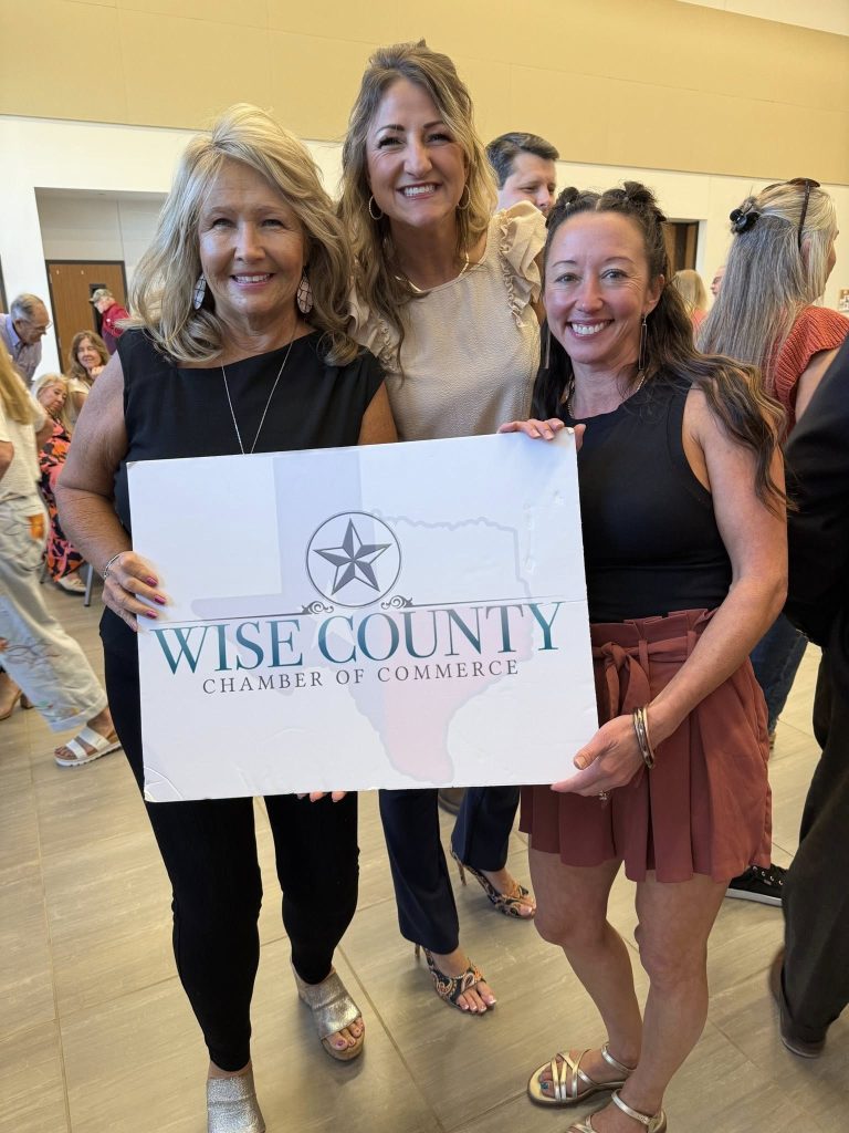 A group of Wise County Chamber of Commerce members and leaders pose together holding the chamber's official logo sign